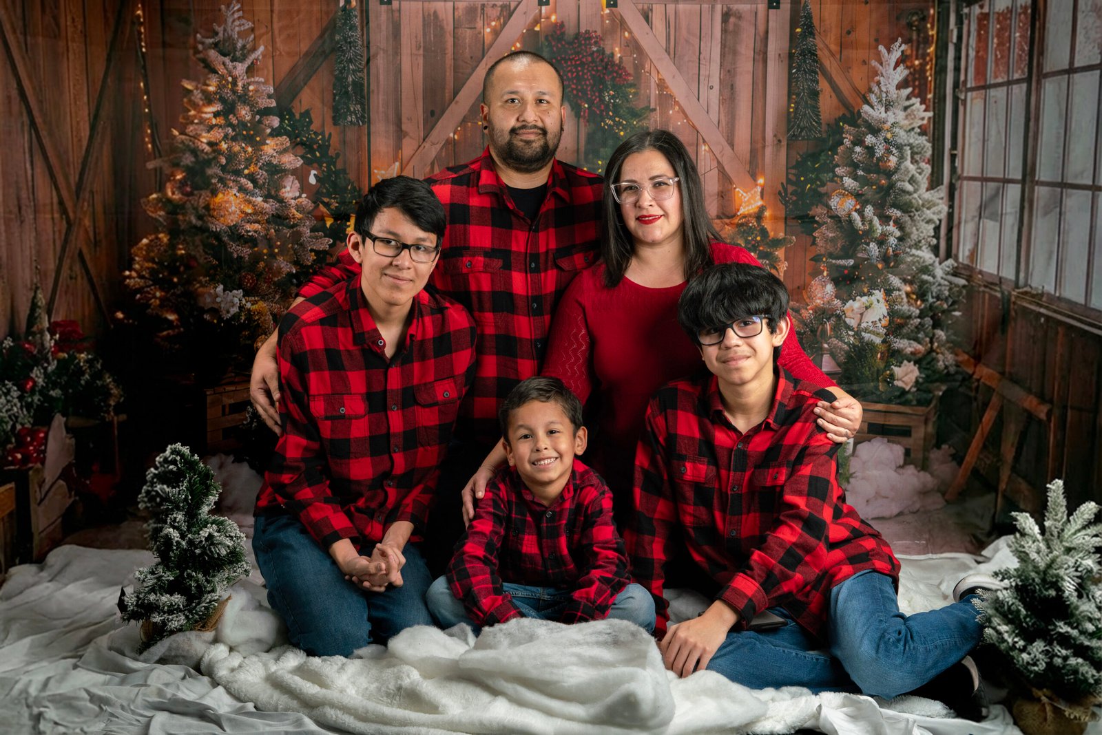 Family of five in red and black plaid posing in a festive Christmas set.