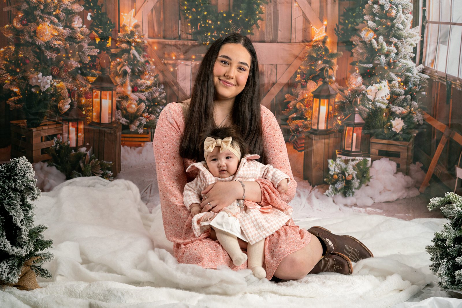 Baby in pink clothes and a headband on a cushion in a snowy holiday scene.