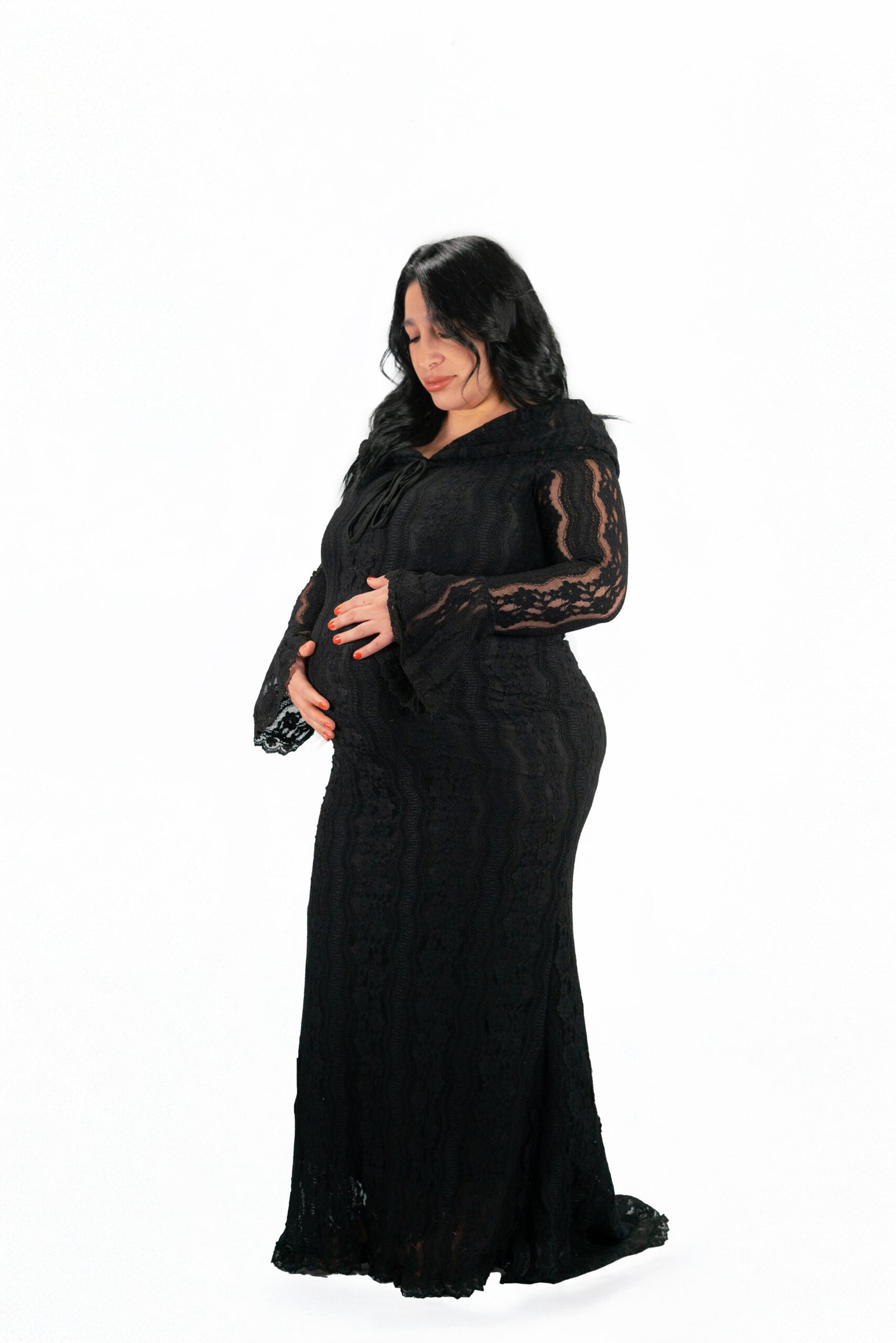 Pregnant woman in a full-length black lace dress against a white studio background.